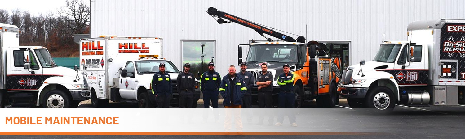 Hill International Truck's mobile repair team standing in front of trucks and a gray building.