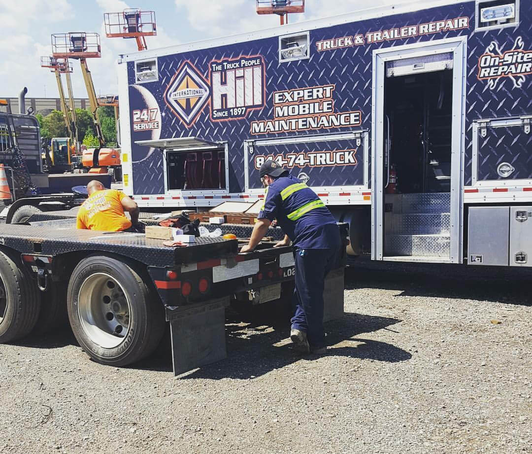 Two mobile maintenance mechanics working on a truck bed in front of a giant blue truck.